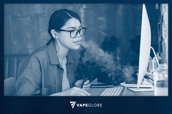 Frau vapt am Arbeitsplatz vor dem PC