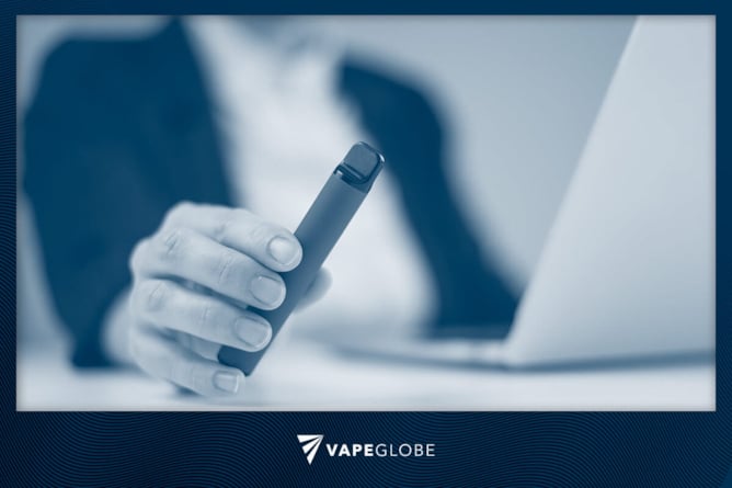 Mann mit Vape sitzt im Büro am Notebook. 