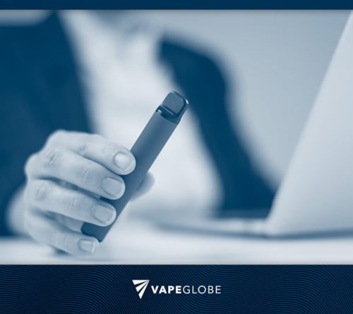 Mann mit Vape sitzt im Büro am Notebook. 