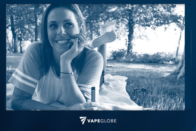 Beim Vaping in der Öffentlichkeit liegt eine Frau auf einer Decke im Park. 