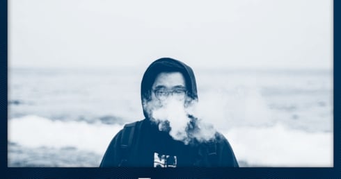 Ein Mann in Kapuzenpullover dampft am Meer,  als Titelbild für den Artikel über häufige Anfängerfehler beim Vapen. 